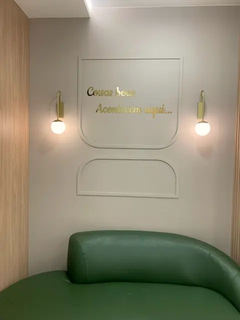 Cantinho da clínica com sofá verde e o lettering dourado Coisas boas acontecem aqui